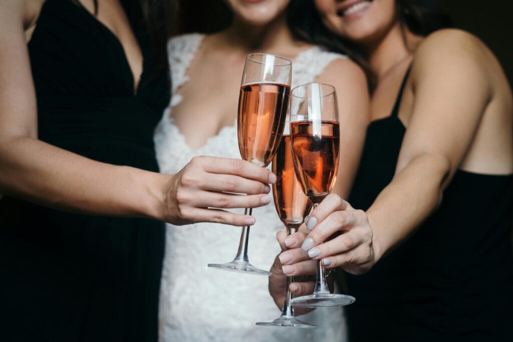 Three women toasting with rose wine glasses in a wedding celebration, captured up close.